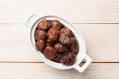 Photo of Roasted edible sweet chestnuts in dish on light wooden table, top view