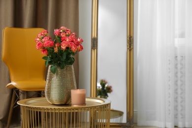 Photo of Bouquet of beautiful roses and burning candle on table indoors, space for text. Interior elements