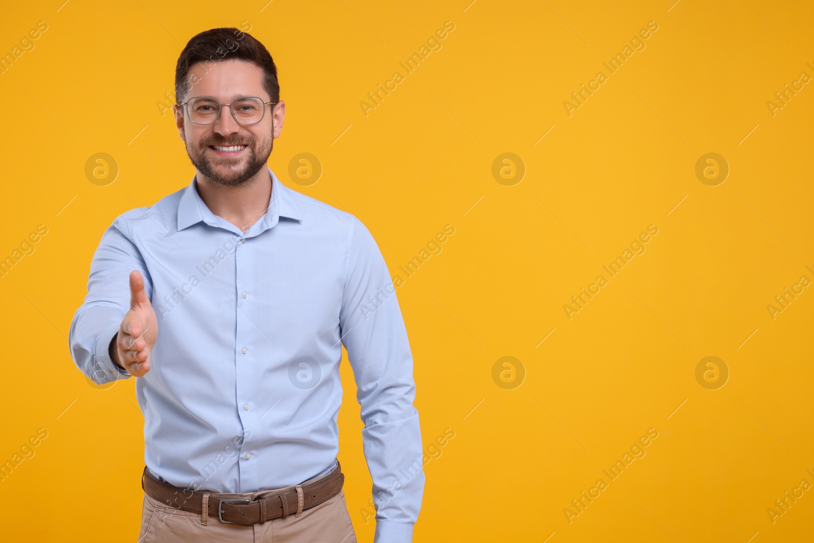Photo of Happy man welcoming and offering handshake on yellow background. Space for text