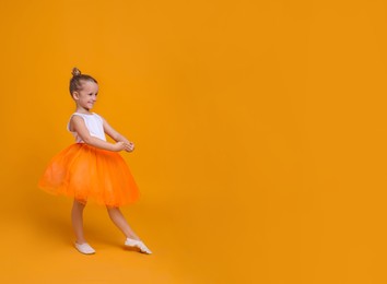 Photo of Cute little girl in tutu skirt dancing on orange background. space for text
