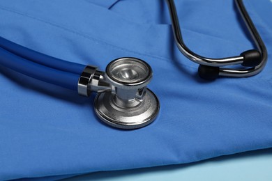 Photo of Medical uniform and stethoscope on light blue background, closeup