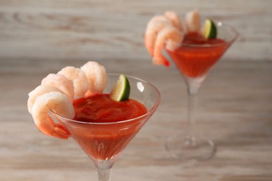 Photo of Tasty shrimp cocktail with sauce in glasses on wooden table, closeup