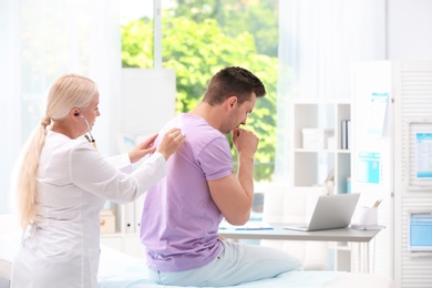 Doctor examining coughing young man at clinic