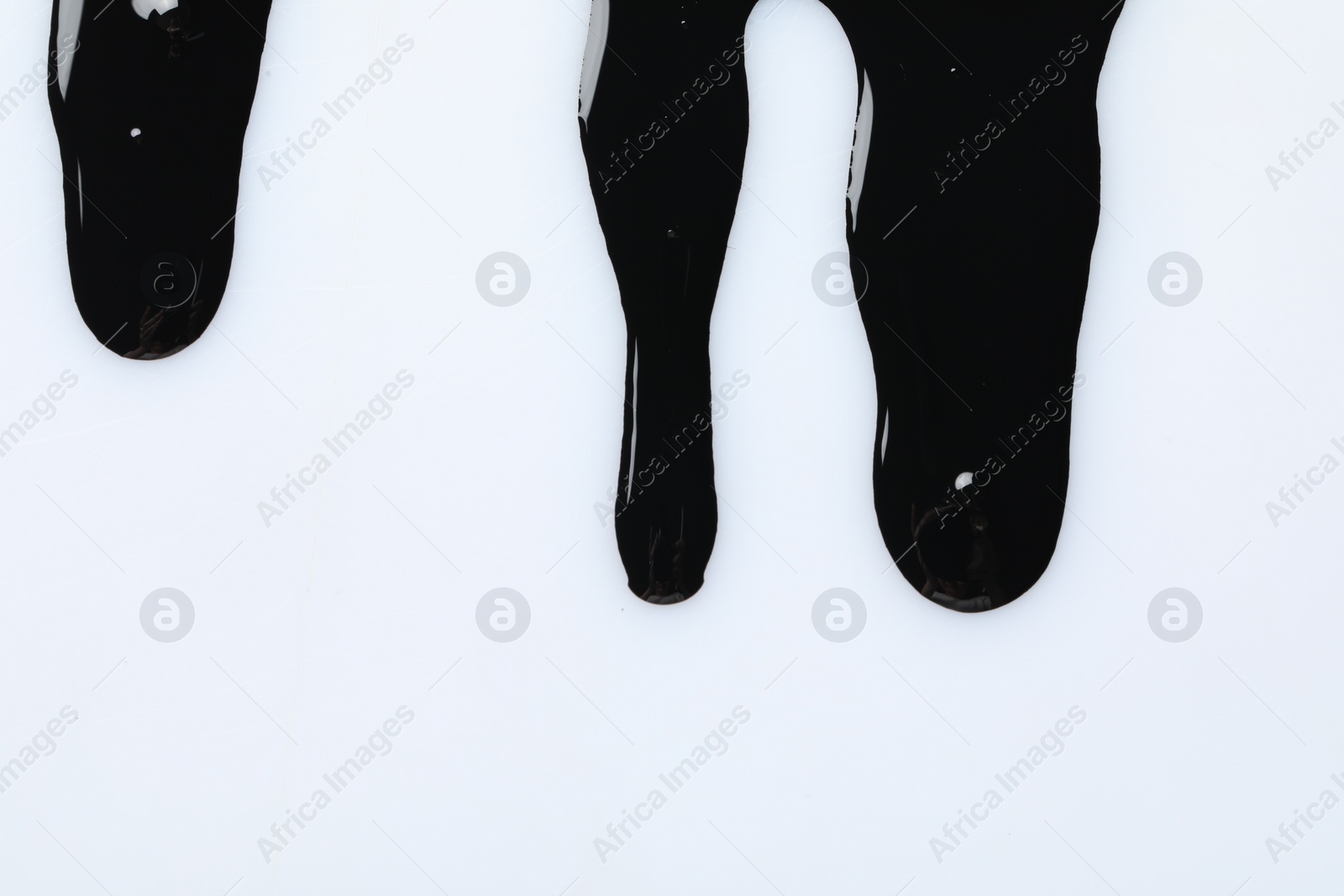 Photo of Black glossy oil flowing on white background