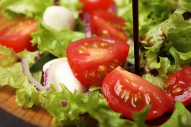 Photo of Pouring balsamic vinegar onto fresh vegetable salad on plate, closeup