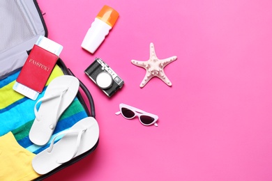 Flat lay composition with suitcase and beach objects on pink background