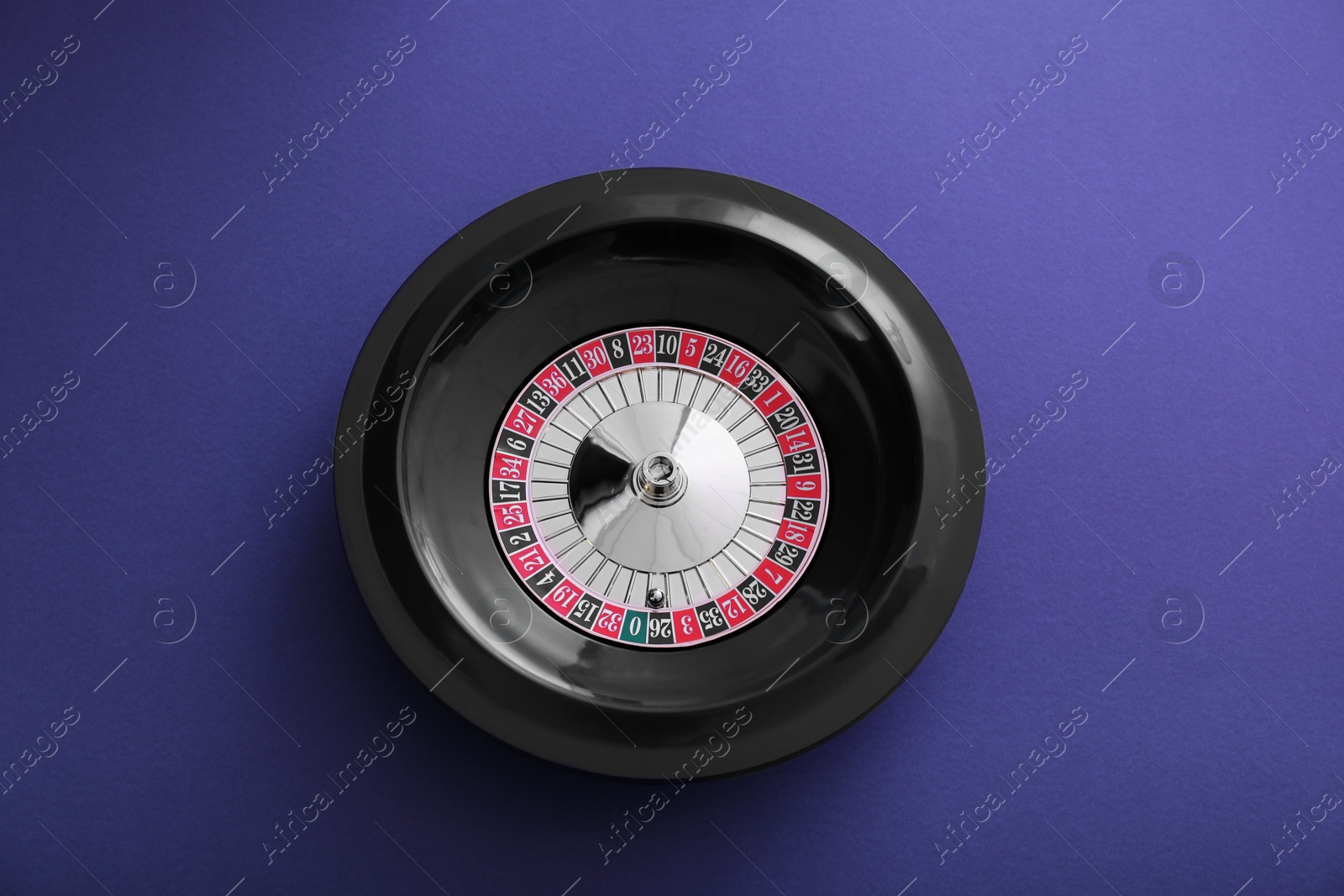 Photo of Roulette wheel with ball on dark violet background, top view. Casino game