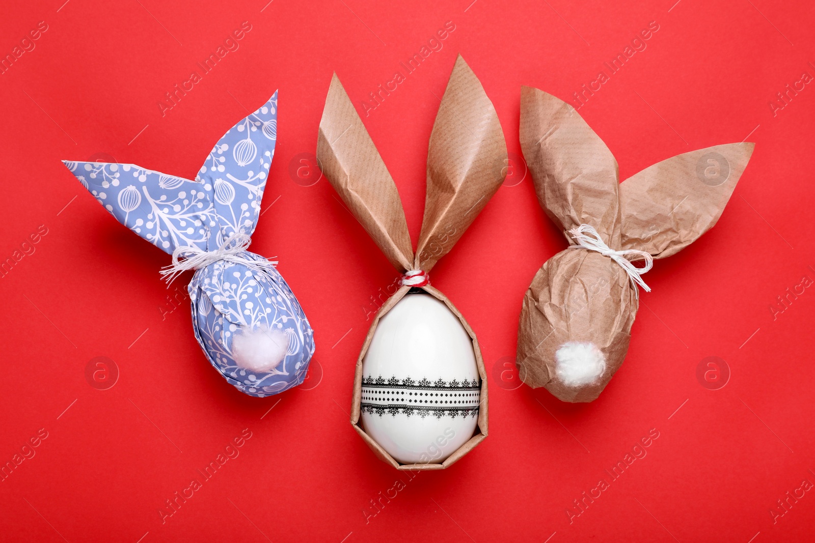 Photo of Easter bunnies made of craft paper and eggs on red background, flat lay