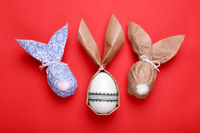 Easter bunnies made of craft paper and eggs on red background, flat lay