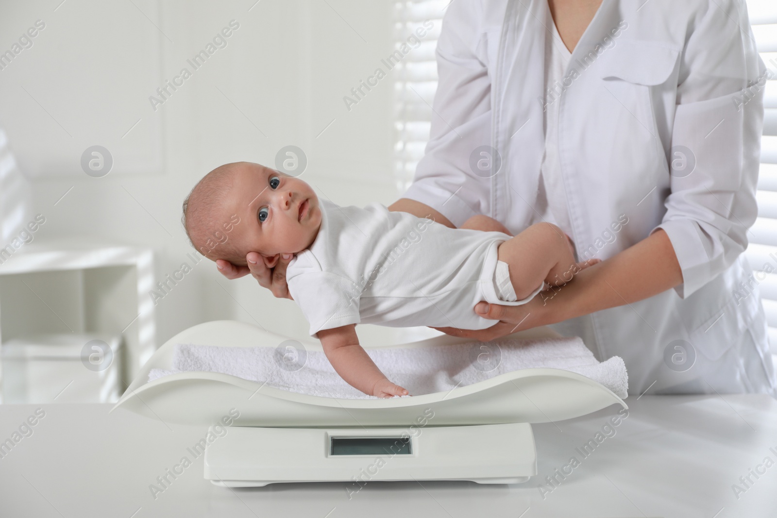 Photo of Doctor weighing cute baby in clinic, closeup