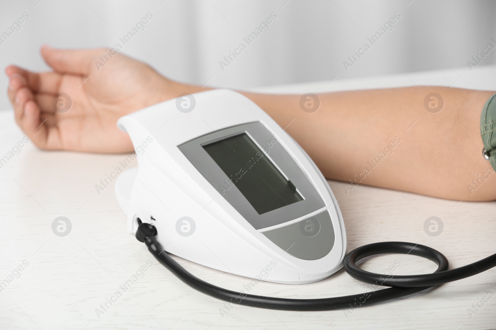 Photo of Woman checking pulse and blood pressure with sphygmomanometer on table, closeup