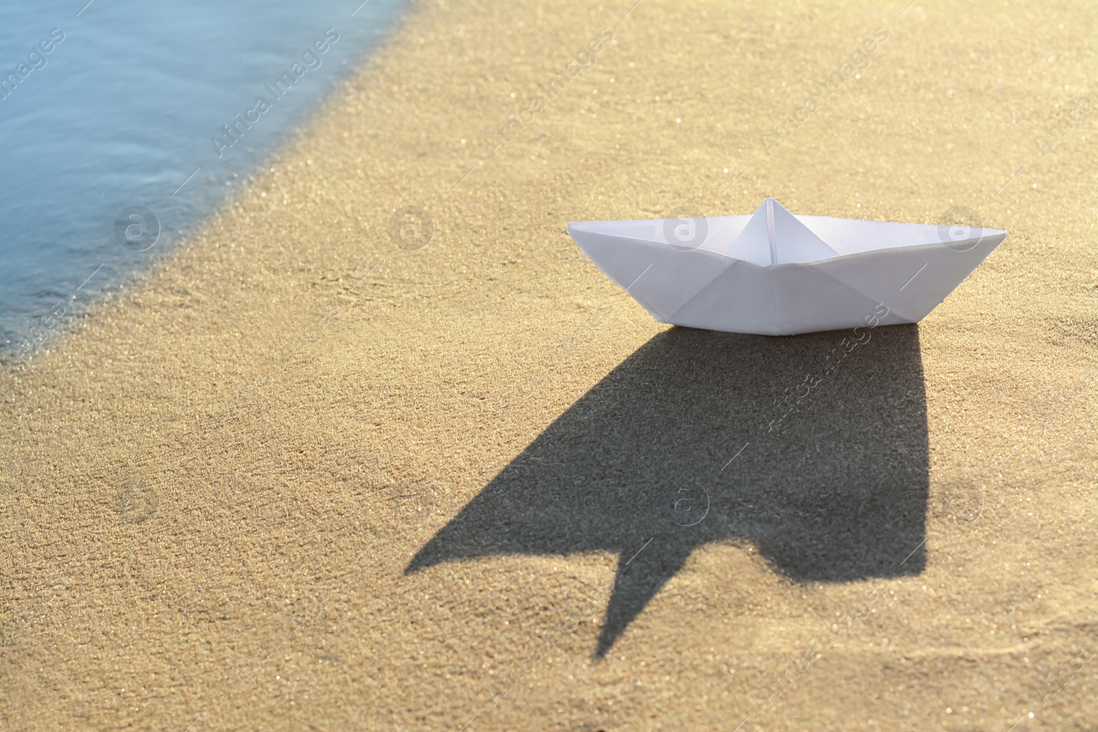 Photo of Beautiful white paper boat on sand near sea, space for text