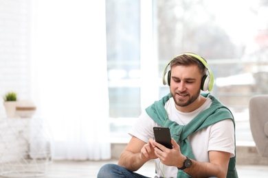 Photo of Young man with headphones and mobile device enjoying music in living room