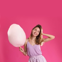 Photo of Happy young woman with cotton candy on pink background