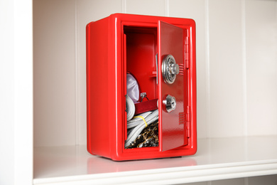 Photo of Open red steel safe with money and jewelry on shelf