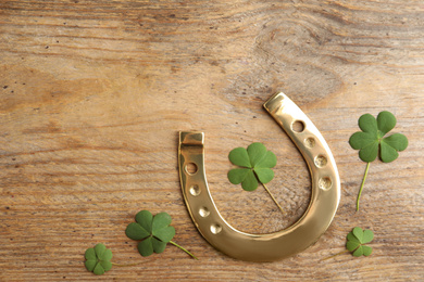 Photo of Clover leaves and horseshoe on wooden table, flat lay. St. Patrick's Day celebration
