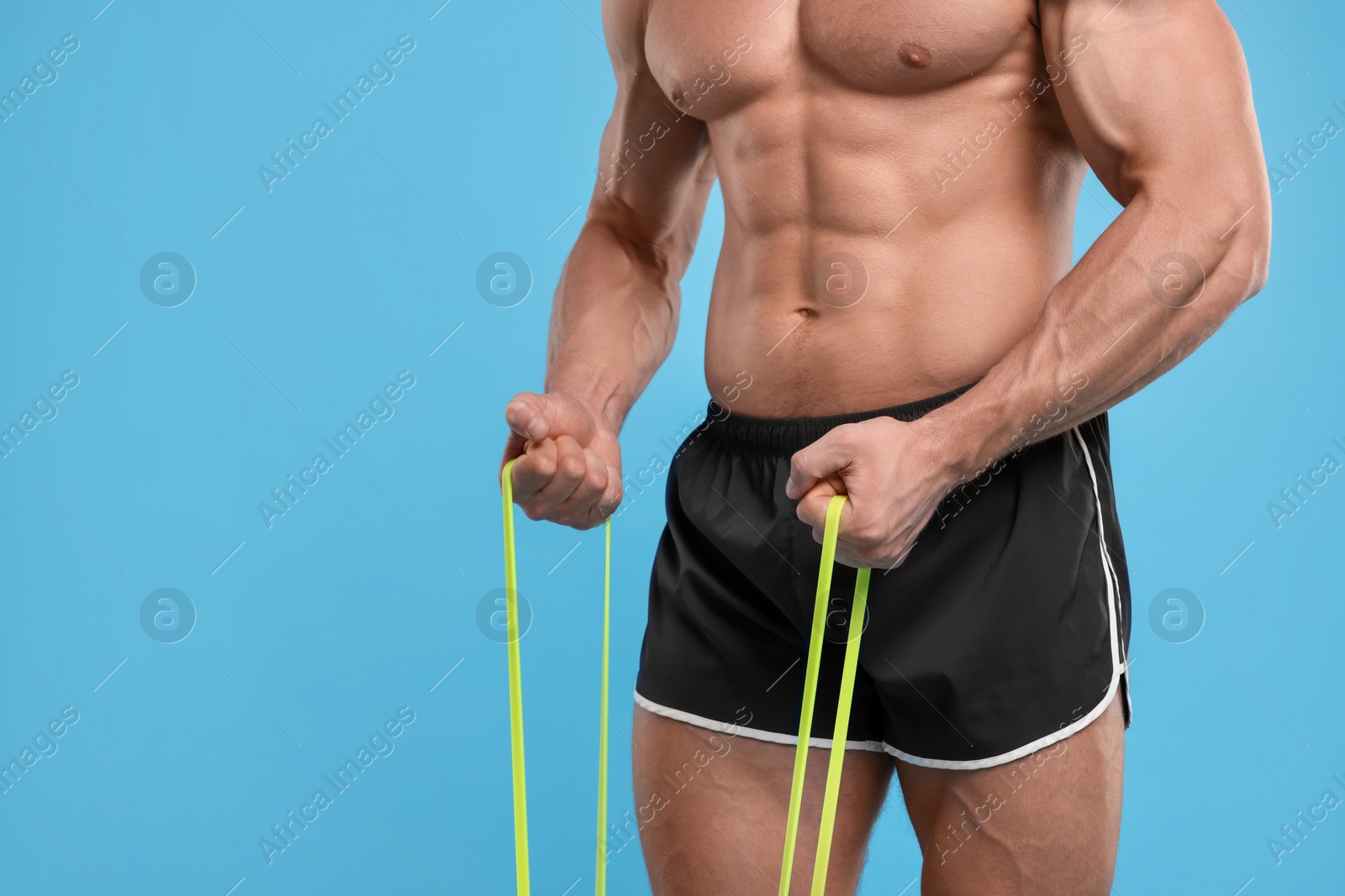 Photo of Young man exercising with elastic resistance band on light blue background, closeup. Space for text
