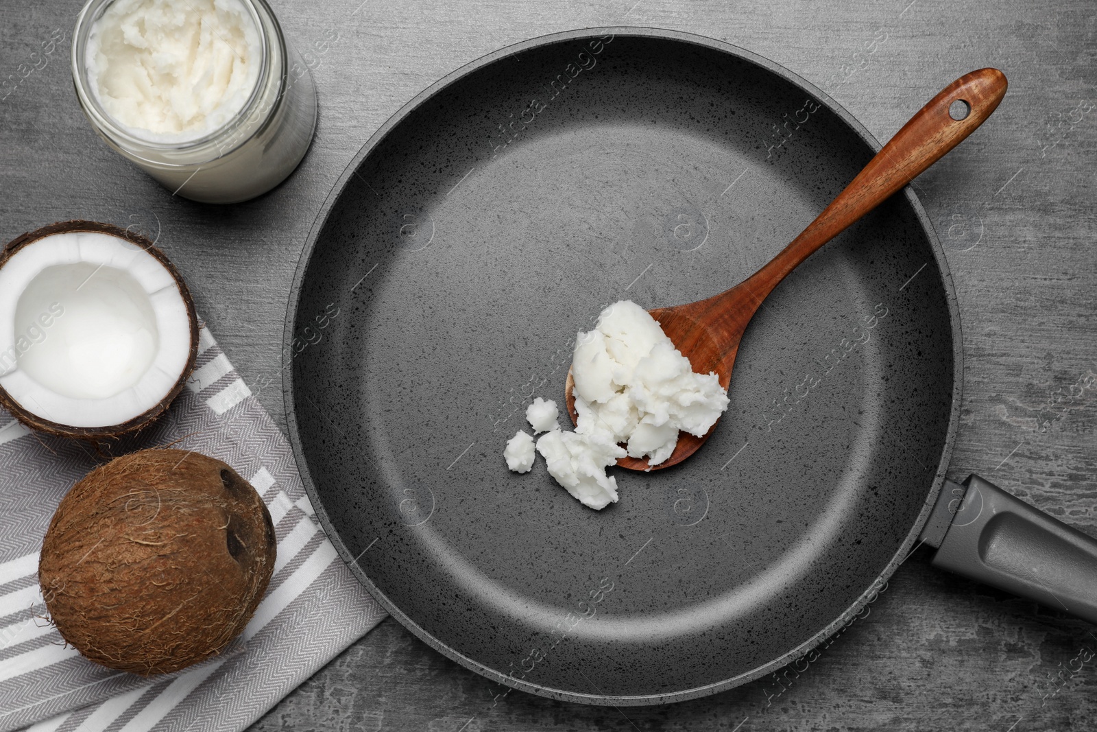 Photo of Frying pan with coconut oil and wooden spoon on grey table, flat lay
