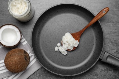 Photo of Frying pan with coconut oil and wooden spoon on grey table, flat lay