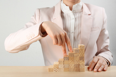 Photo of Businesswoman and stairs made with blocks on wooden table, closeup. Career promotion concept