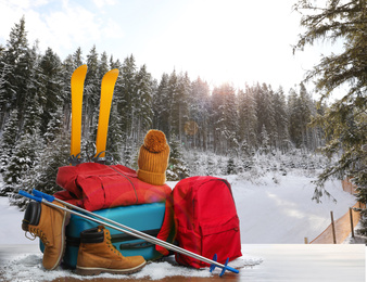 Image of Suitcase with warm clothes on wooden surface against beautiful winter landscape