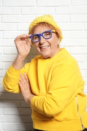 Portrait of elderly woman in hipster outfit near brick wall