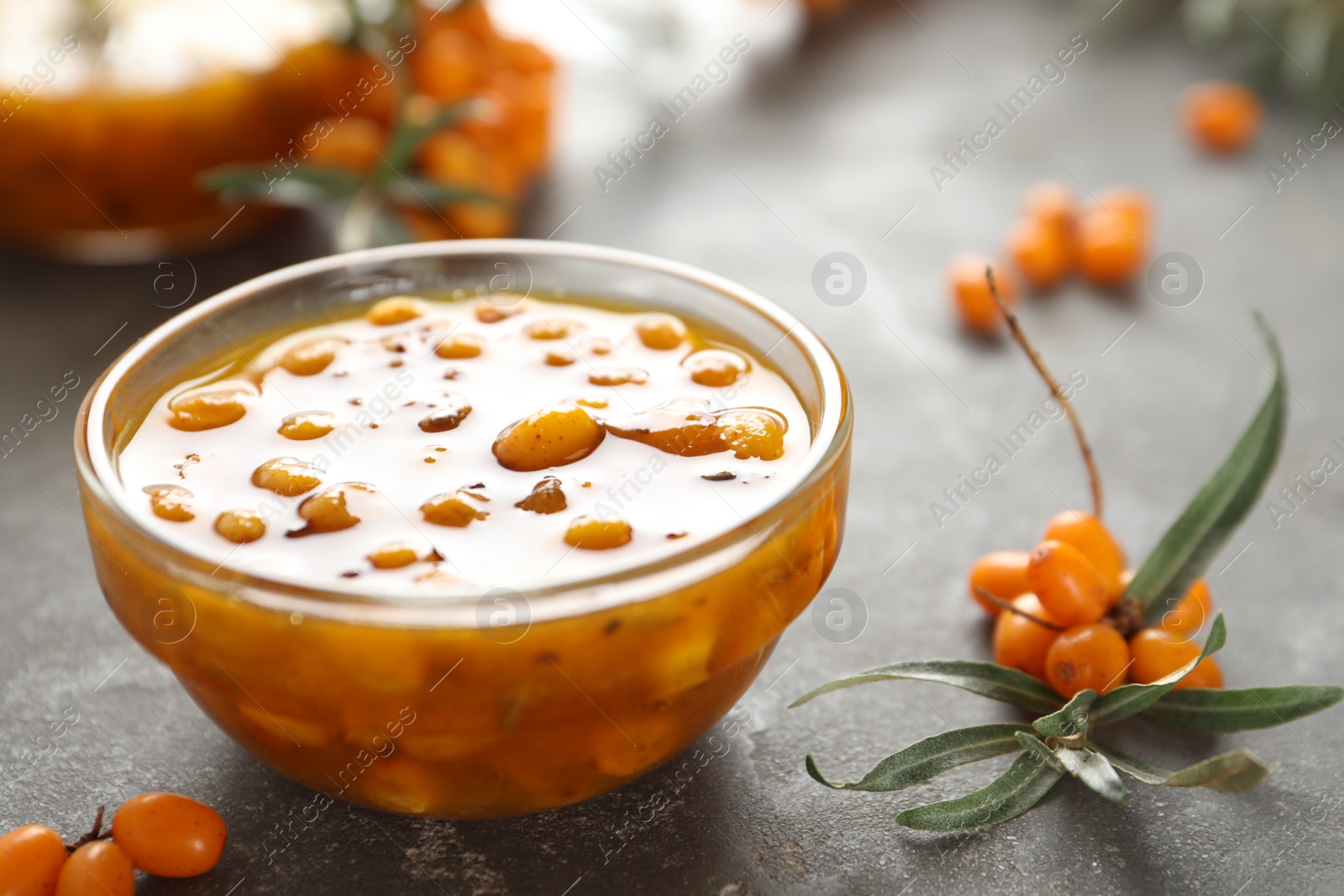 Photo of Delicious sea buckthorn jam and fresh berries on grey table, closeup