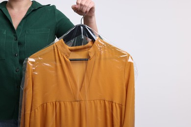 Photo of Dry-cleaning service. Woman holding dress in plastic bag on white background, closeup. Space for text