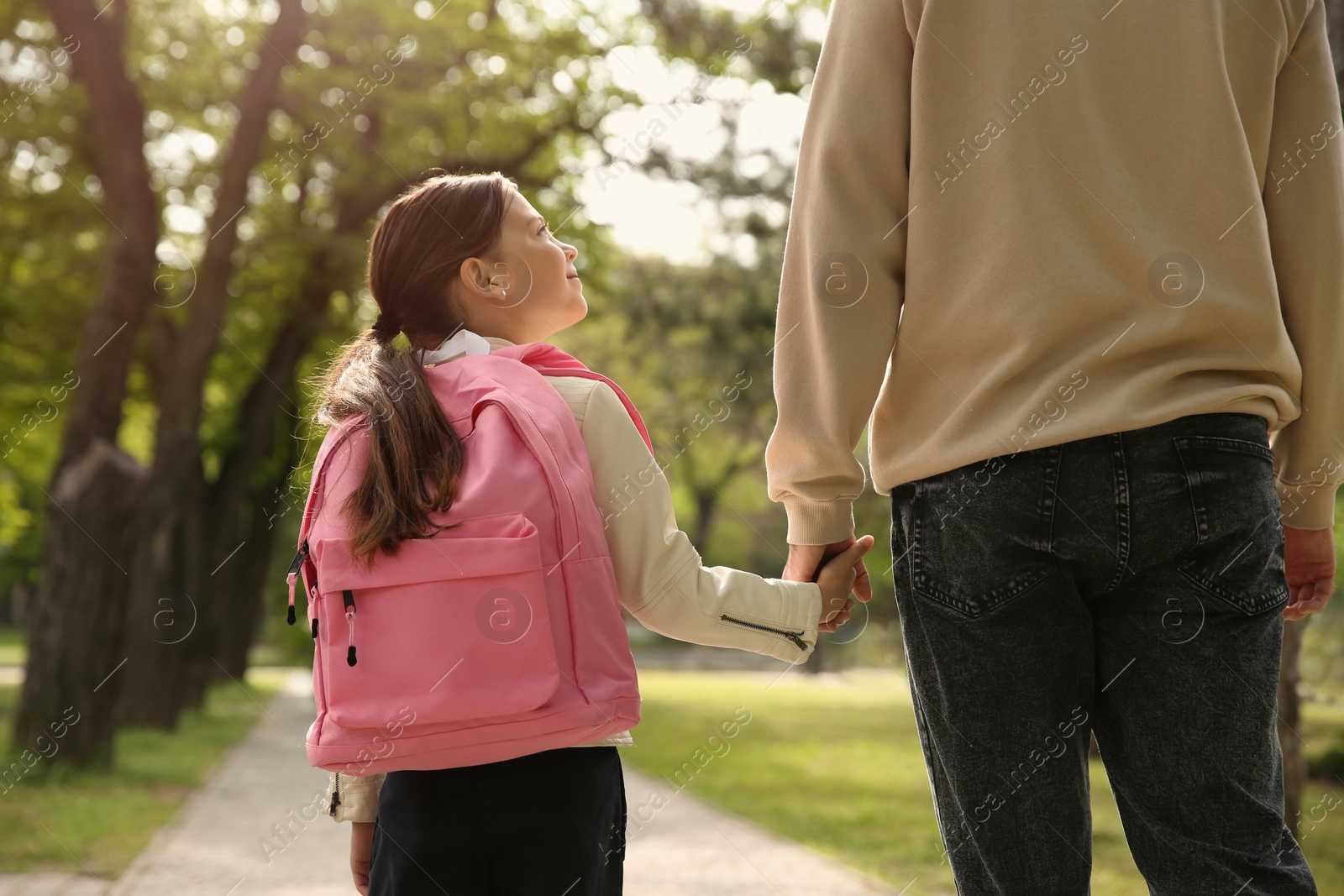 Photo of Father taking his little daughter to school through park, back view