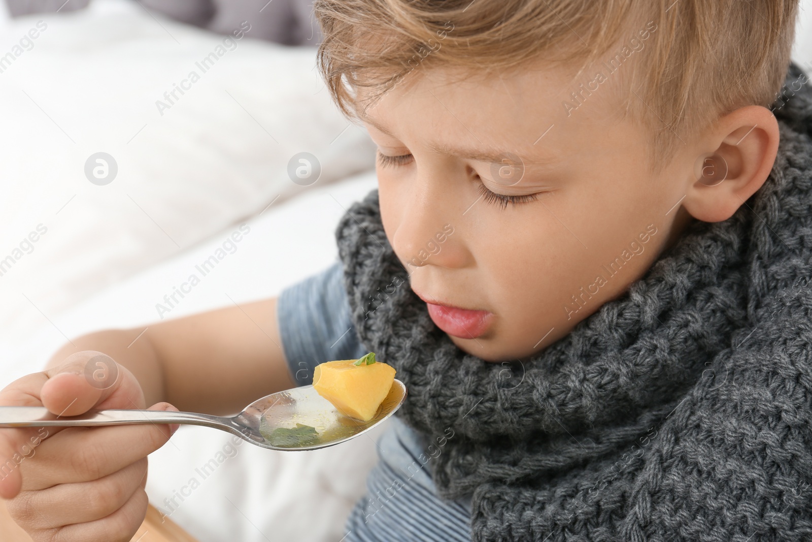 Photo of Sick little boy eating broth to cure cold in bed at home