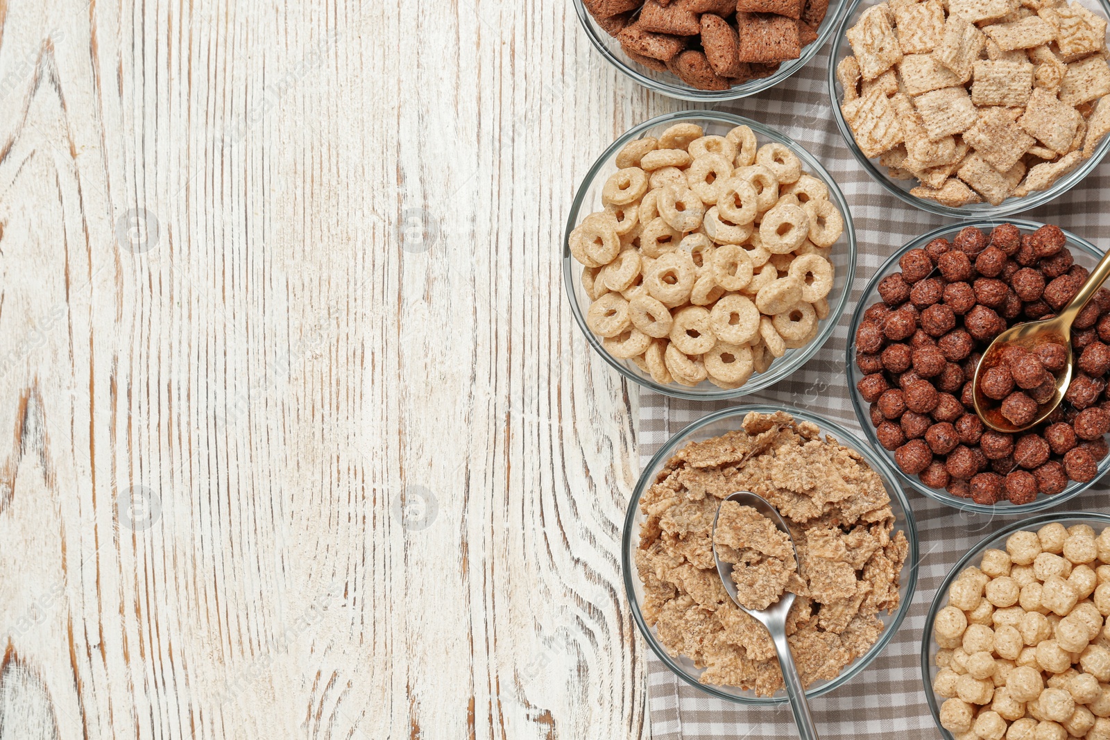 Photo of Different breakfast cereals in glass bowls on white wooden table, flat lay. Space for text