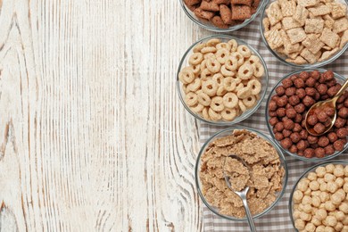 Photo of Different breakfast cereals in glass bowls on white wooden table, flat lay. Space for text