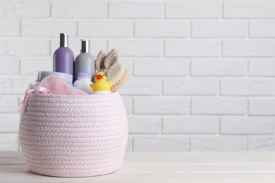 Photo of Basket full of different baby cosmetic products, accessories and toys on white wooden table. Space for text