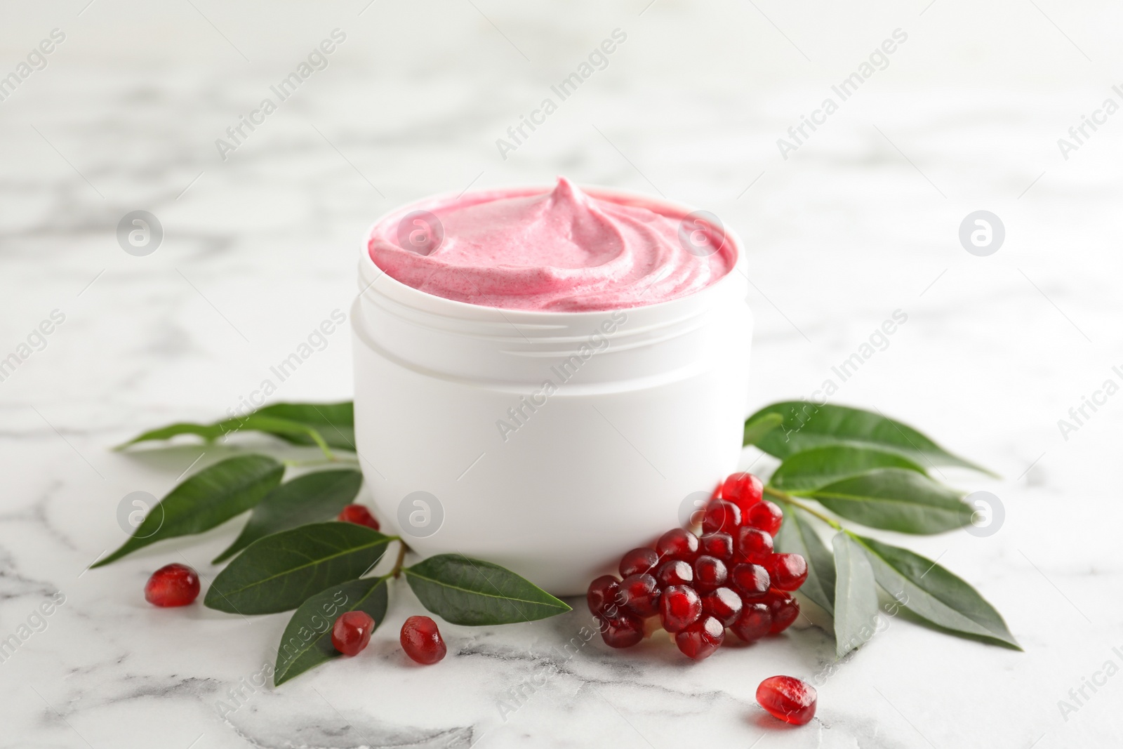 Photo of Fresh pomegranate and jar of facial mask on white marble table, closeup. Natural organic cosmetics