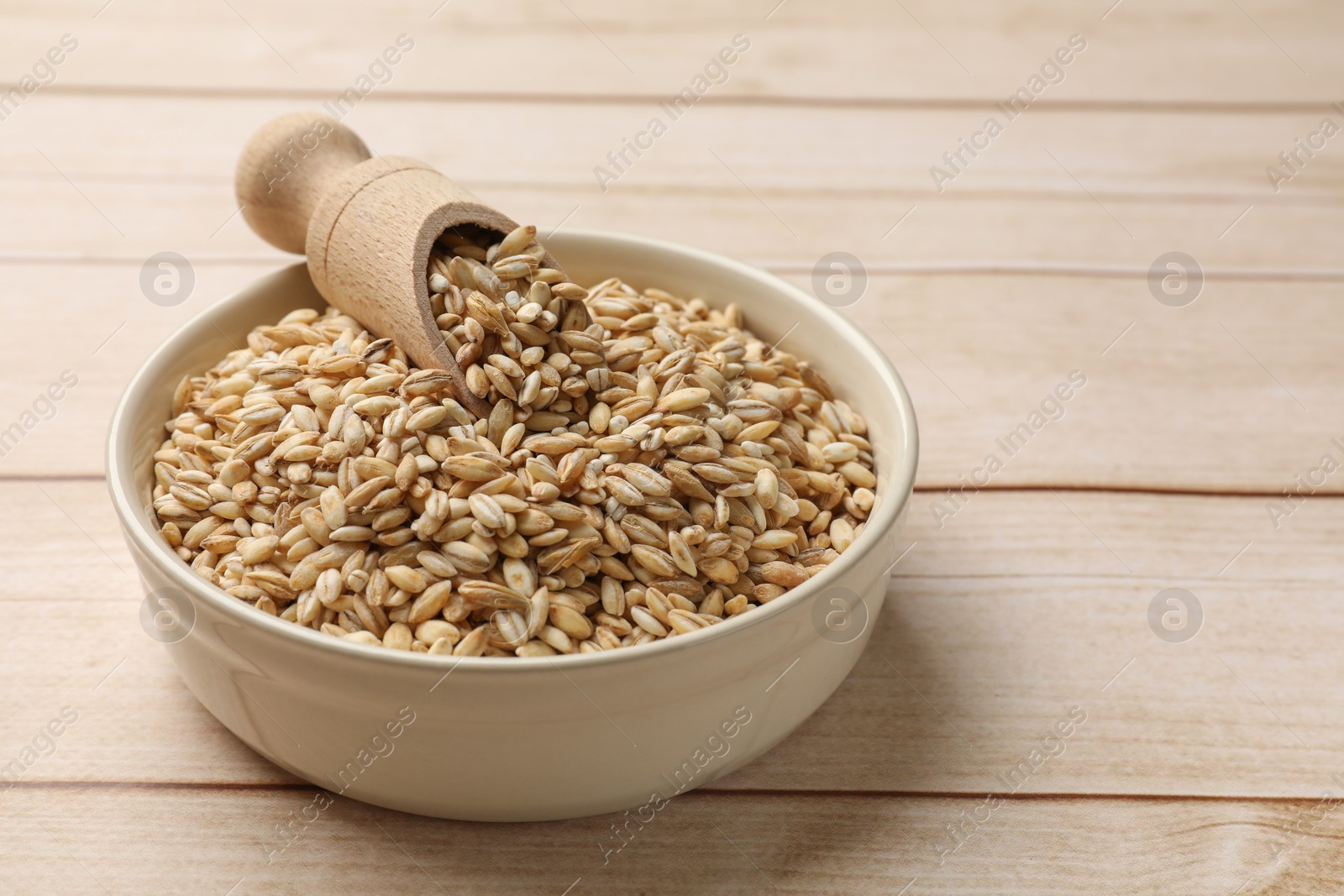 Photo of Dry pearl barley in bowl and scoop on light wooden table, space for text