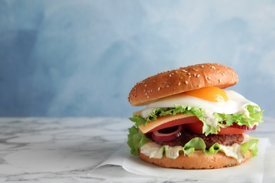 Photo of Tasty burger with fried egg on marble table against color background, space for text