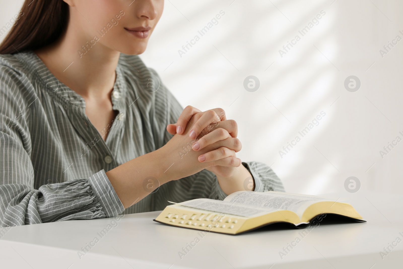 Photo of Religious woman praying over Bible at table indoors, closeup