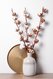 Vase with bouquet of cotton branches on wooden table against white background