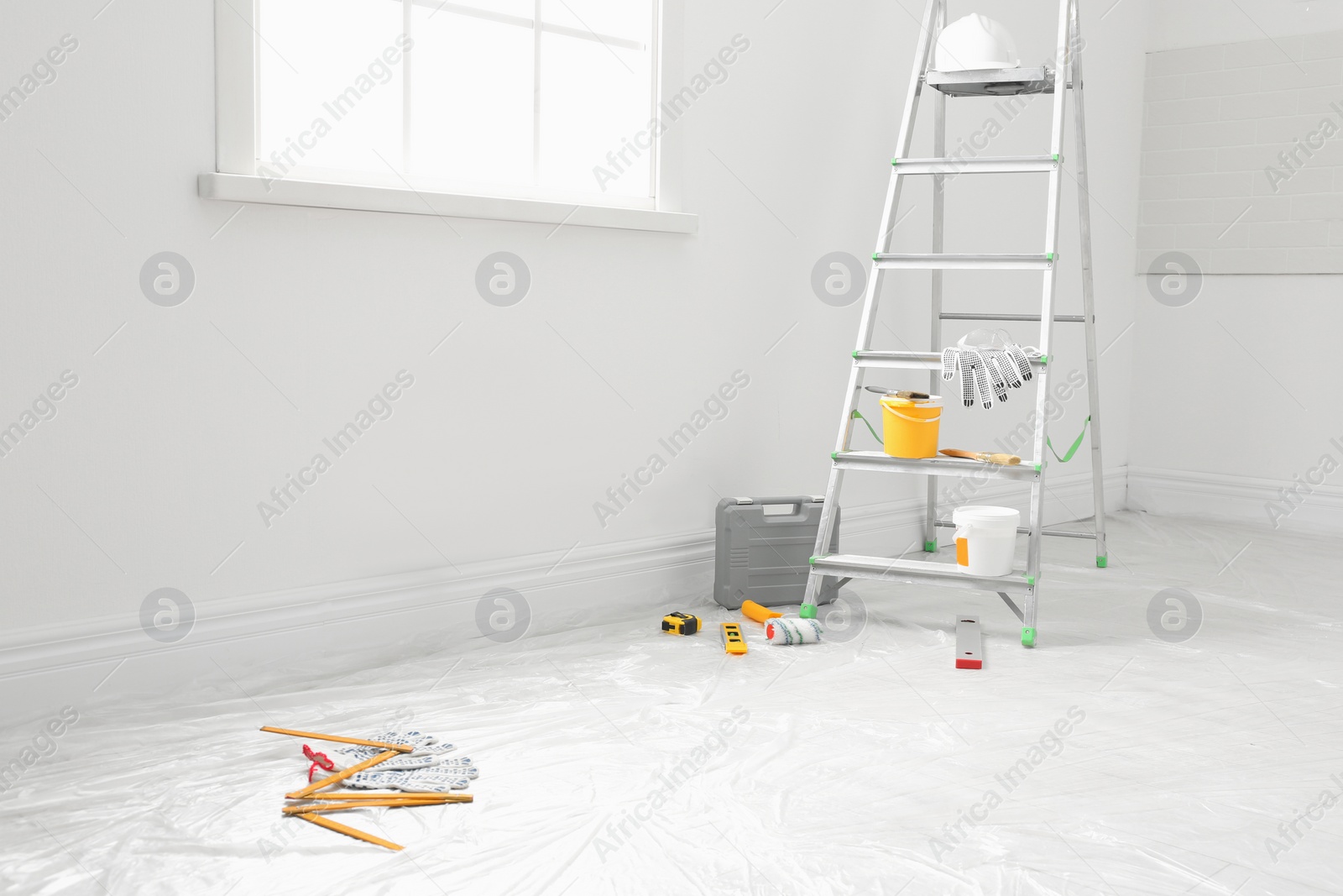 Photo of Stepladder and different tools near wall in room. Interior renovation