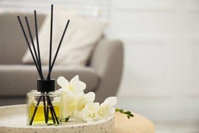 Photo of Reed diffuser with freesia on table in living room. Space for text