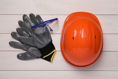 Hard hat, goggles and gloves on white wooden table, flat lay. Safety equipment
