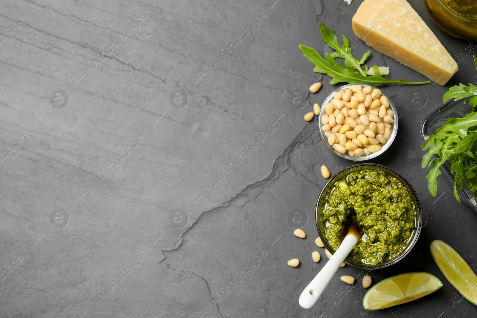 Photo of Bowl of tasty arugula pesto and ingredients on black table, flat lay. Space for text