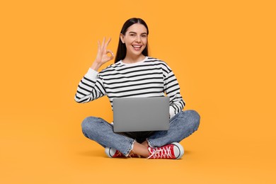 Photo of Happy woman with laptop showing OK gesture on orange background