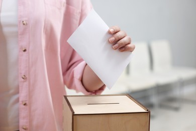 Photo of Woman putting her vote into ballot box on blurred background, closeup