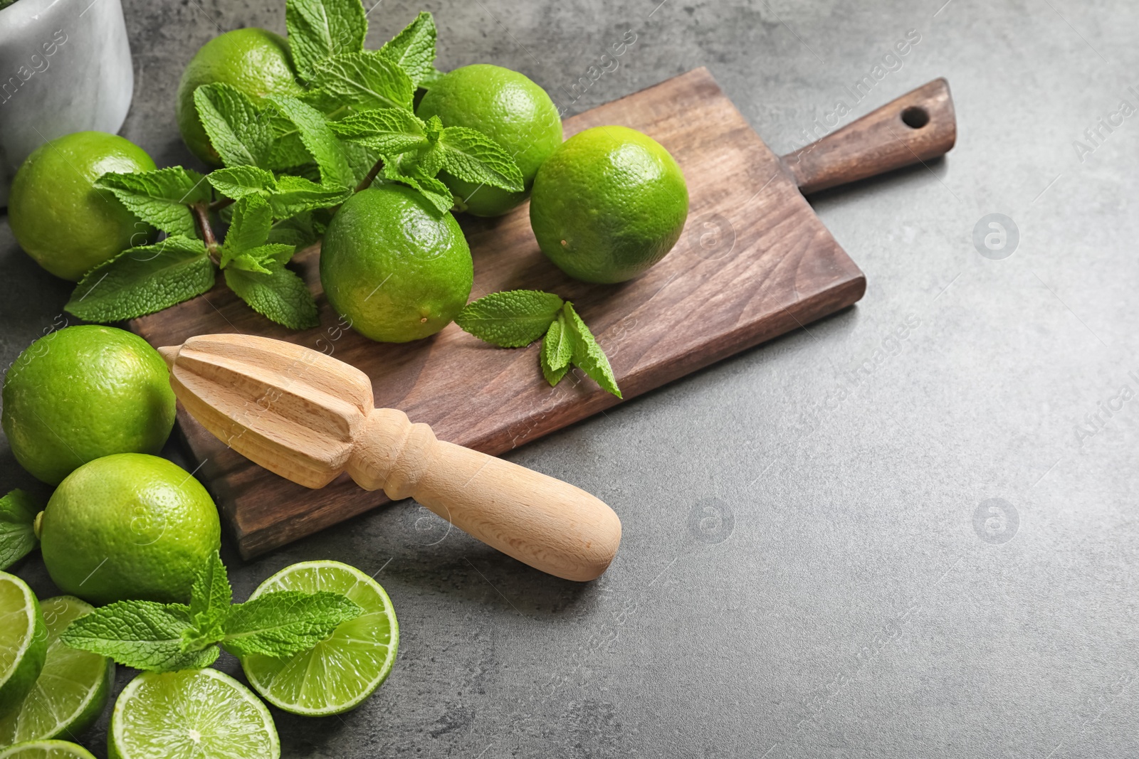 Photo of Composition with ripe limes, mint and juicer on grey background. Refreshing beverage recipe