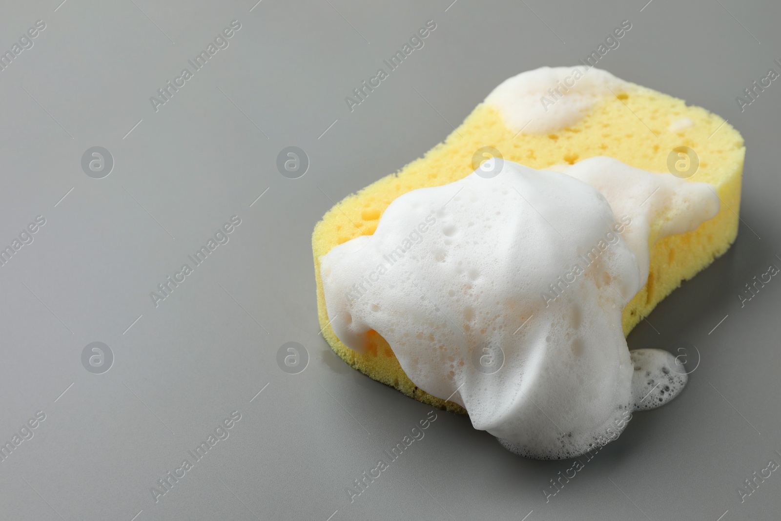 Photo of Yellow sponge with foam on grey background, closeup. Space for text