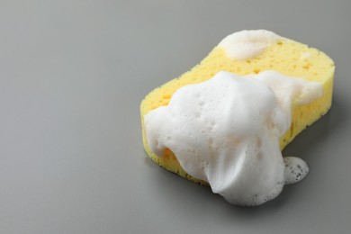 Yellow sponge with foam on grey background, closeup. Space for text