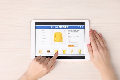 Woman with tablet shopping online at white wooden table, top view