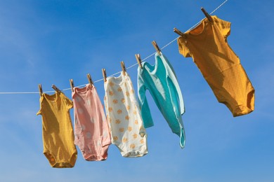 Photo of Clean baby onesies hanging on washing line against sky. Drying clothes