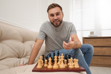 Photo of Happy young man playing chess on sofa at home